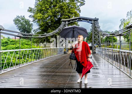 Una donna anziana con un ombrello cammina attraverso lo storico ponte sospeso di Ozimek, in Polonia, in una giornata di pioggia. Foto Stock