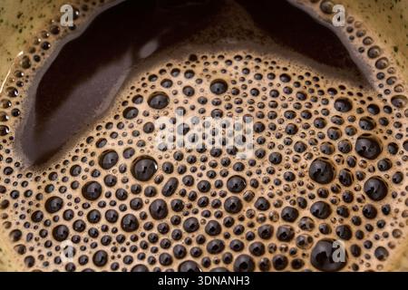 Bolle di schiuma di caffè che formano una superficie ruvida con liquido scuro Foto Stock