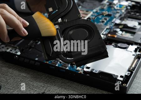 Una mano utilizza una spazzola per pulire le parti interne di un computer portatile. Il notebook è aperto e mostra vari componenti. Foto Stock