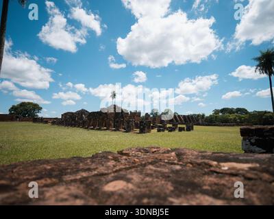 Paesaggio orizzontale di un campo erboso con vecchie strutture in rovina sullo sfondo sotto un cielo blu con nuvole. Utile per turismo, storia, patrimonio Foto Stock
