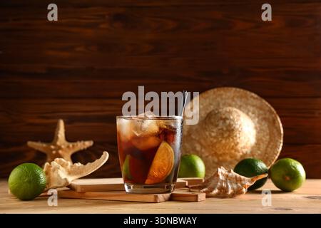 Bicchiere di cocktail Cuba Libre freddo con conchiglia e stelle marine su sfondo di legno Foto Stock