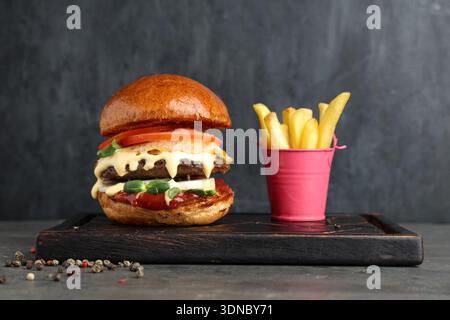Tavola di legno con gustosi hamburger, patatine fritte e peperoni su sfondo grunge nero Foto Stock
