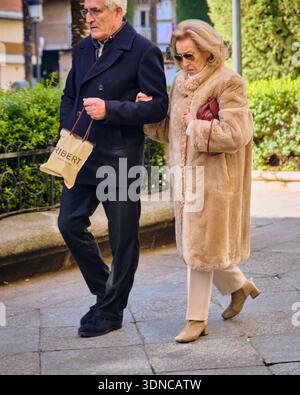 Una coppia di anziani cammina con il braccio in una strada a Salamanca in Spagna a dicembre indossando cappotti invernali e portando con sé una borsa della spesa compagnia e urbana Foto Stock