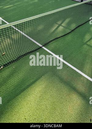Padel o campo da tennis con linee bianche. Ripresa ad angolo alto di un campo sportivo in erba verde con rete nera e fascia superiore bianca. Foto Stock