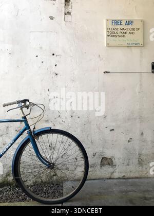 Una bicicletta Triumph d'epoca si appoggia contro un muro battuto dal tempo e presenta una stazione pubblica "Free Air" e una stazione di attrezzi per biciclette in Scozia, Regno Unito. Foto Stock