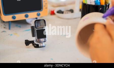 Influencer che crea contenuti per workshop artistici con una action camera, ambientata su un tavolo artistico. Messa a fuoco selettiva sul soggetto. Foto Stock