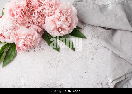 Bouquet di fiori di peonia rosa corallo e tovagliolo di lino grigio su sfondo di pietra grunge. Biglietto d'invito o di compleanno in stile vintage. Foto Stock