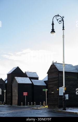 Tradizionali capanne nere per la pesca con una leggera spolveratura di neve alla luce del sole invernale, Hastings Old Town, East Sussex, Inghilterra, Regno Unito. Foto Stock