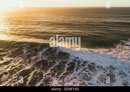 Vista aerea della luce dorata del sole che baciano le onde schiumose mentre un surfista cavalca la cresta, Bidart, Nouvelle-Aquitaine, Francia. Foto Stock