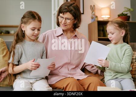 Donna di mezza età seduta con due ragazze che condividono disegni Foto Stock