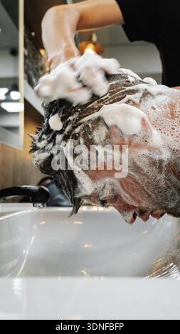 Uomo che viene lavato i capelli in un salone nel pomeriggio con acqua e sapone Foto Stock