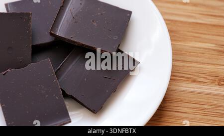 Pezzi di cioccolato fondente rotti su un piatto bianco. Primo piano. Foto Stock