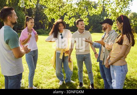 Gruppo di giovani adulti multietnici in piedi insieme, chiacchierando e gestendo, impegnandosi in conversazione Foto Stock