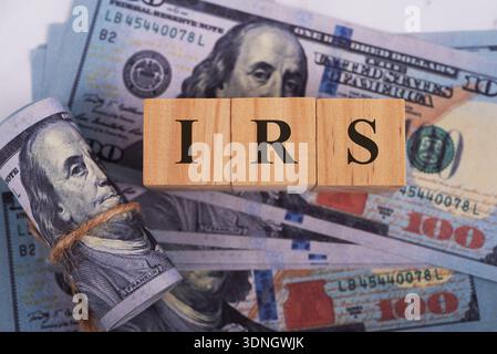 Blocco di legno con testo IRS e concetto finanziario di banconote in dollari americani Foto Stock