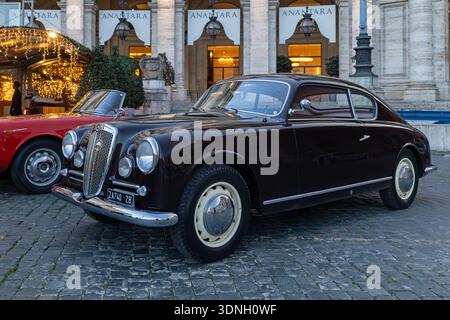 Roma, Italia - 17 gennaio 2026: Un'elegante Lancia Aurelia B20 GT parcheggiata sui ciottoli di Piazza della Repubblica, incorniciata dalla calda bugia serale Foto Stock