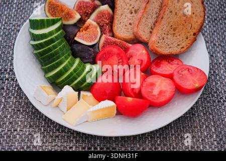 Un piatto nutriente e colorato per la colazione con fichi freschi a fette, cetrioli, pomodori ciliegini, cremoso formaggio brie e pane rustico, magnificamente Foto Stock