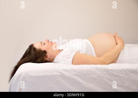 donna incinta che dorme sul suo letto a casa Foto Stock
