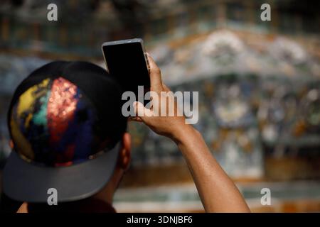 Turista maschile che indossa un berretto in piedi che scatta una foto con uno smartphone, texture della pelle della mano, vista posteriore Foto Stock