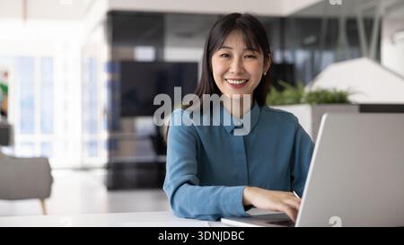 Felice giovane donna d'affari asiatica che scrive sul laptop Foto Stock