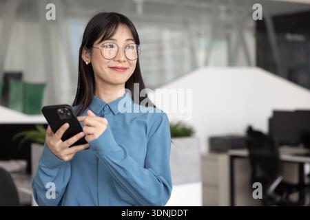 Felice giovane asiatico project manager donna in occhiali con smartphone Foto Stock