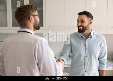 Felice sorridente giovane paziente maschio stringe la mano a un medico di fiducia Foto Stock