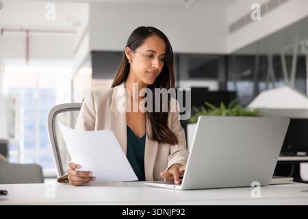 Donna d'affari concentrata che lavora con i documenti e lavora con un notebook in ufficio Foto Stock