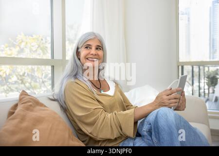 Donna felice che riflette guarda da parte con un tablet in mano Foto Stock