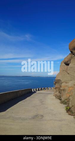 Strada costiera panoramica accanto a massicce formazioni rocciose di basalto che si affacciano sull'oceano blu sotto un cielo limpido nelle isole Penghu, Taiwan. Foto Stock