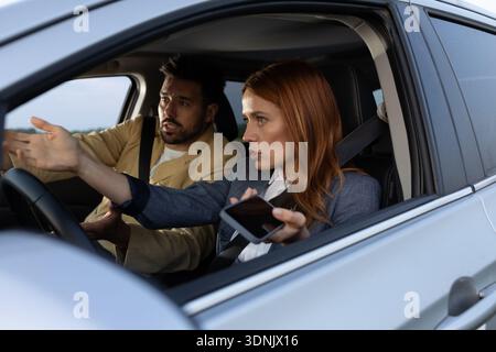 Una giovane coppia che ha un disaccordo mentre è seduta in macchina. Donna e uomo tengono le mani in alto indicando la strada con espressioni preoccupate e arrabbiate Foto Stock