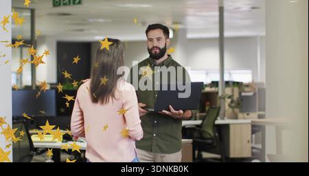 Con un laptop, un uomo barbuto che spiega il progetto a una collega donna in un ufficio open space, stelle d'oro Foto Stock