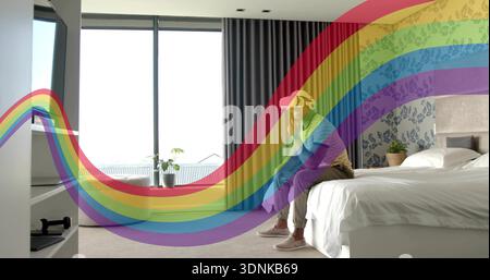 Tenendo in mano un uomo che indossa un cappellino da baseball, seduto sul letto accanto alla finestra con rivestimento arcobaleno, spazio per fotocopie Foto Stock