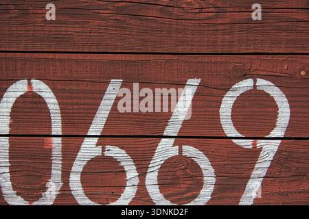 Numeri bianchi incisi su una superficie in legno rossa intemprata Foto Stock