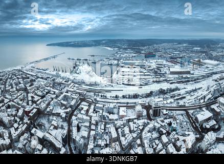 Vista aerea invernale dal drone di Snowy City e degli edifici industriali, Sea Port Varna Harbor with Cranes, costa del Mar Nero Bulgaria Foto Stock