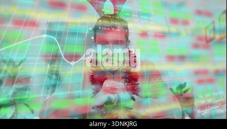 Uomo maturo seduto in maglione rosso, tinsel e cappello a cono in ufficio con sovrapposizione dati di mercato Foto Stock