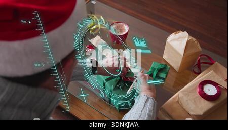 Avvolgere l'uomo con il cappello di Babbo Natale e il maglione manipolando il nastro al tavolo di vetro con l'HUD olografico AR Foto Stock
