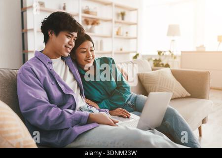 Concetto di passatempi per il fine settimana. Sposato giovane coppia asiatica usando il portatile a casa, rilassarsi sul divano insieme, spazio copia Foto Stock