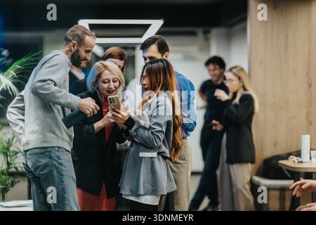 Gruppo di colleghi che condividono un momento con uno smartphone in un ufficio moderno Foto Stock