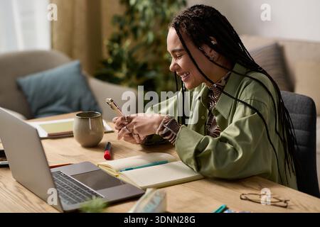In un appartamento elegante, una giovane donna con trecce sorride mentre usa il telefono. Foto Stock