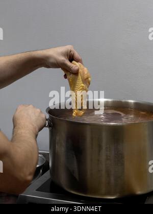 Lo chef prepara un brodo di pollo in una pentola di acciaio inossidabile, preparando una base per zuppa Foto Stock