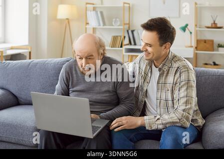 Senior con computer portatile, figlio adulto, nipote adulto e padre anziano che imparano a utilizzare l'app Foto Stock