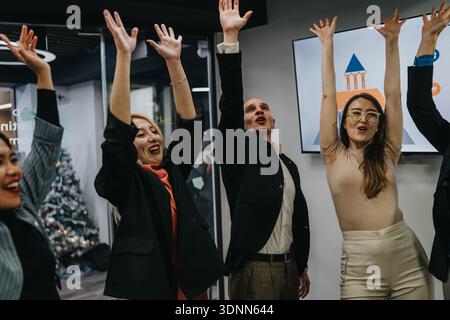 Festeggiamenti di squadra in un ufficio moderno, mentre tutti alzano la mano con allegria e spirito festivo Foto Stock