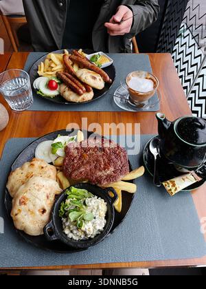 Tradizionale pasto alla griglia dei Balcani servito in un ristorante con salsicce alla griglia, polpettine di manzo pljeskavica, patatine fritte, focaccia, insalata, e caffè su un legno Foto Stock