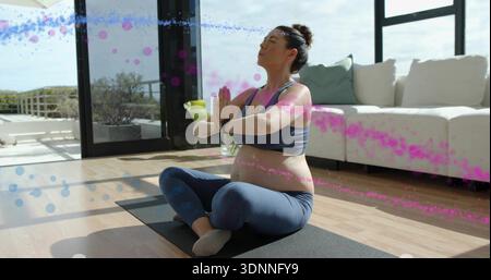 Donna incinta seduta che pratica yoga prenatale in soggiorno, indossa abbigliamento sportivo navy, tappetino nero Foto Stock