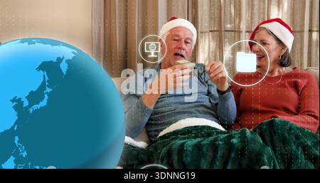 Una coppia anziana seduta nei cappelli di Babbo Natale con tazza e teabag sul divano, con interfaccia utente Blue Globe Foto Stock