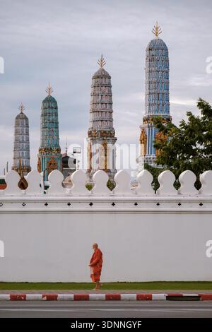 Bangkok, Thailandia, 19 novembre 2025, Un monaco vestito con le tradizionali vesti arancioni cammina piacevolmente davanti a suggestive guglie del tempio adornate da intricati motivi del Wat Phra kaeo. Foto Stock