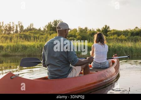 Uomo e donna fanno kayak insieme su un lago circondato da alberi e acqua. Condividono un momento di avventura nella natura. Foto Stock