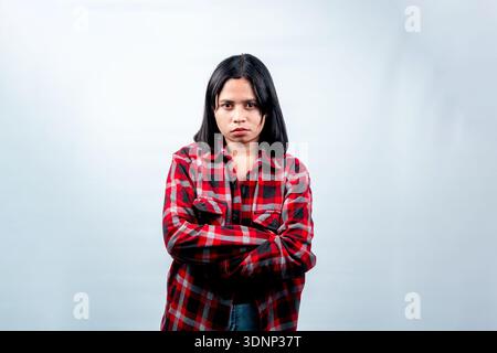 Ritratto di una donna indonesiana frustrata con una camicia di flanella rossa in piedi con le braccia incrociate e un volto scontroso, isolato sul bianco. Foto Stock