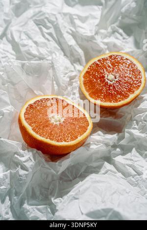 Due vivaci metà pompelmo sono posizionate ad arte su carta bianca testurizzata, catturando la luce naturale per enfatizzare la polpa succosa. Questa composizione com Foto Stock