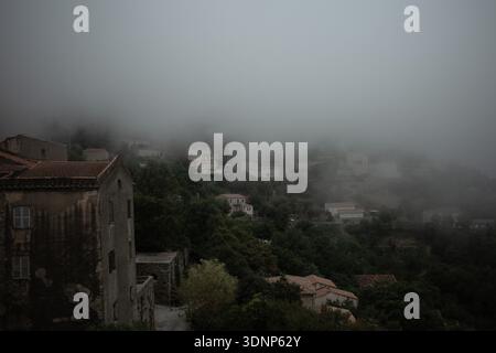 Villaggio collinare di Speloncato in Corsica, case in pietra e tetti in terracotta che emergono attraverso la bassa nebbia di montagna. Foto Stock