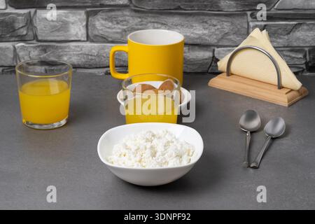 Succo d'arancia, caffè, muffin e formaggio fresco sul tavolo contro la pietra grigia Foto Stock